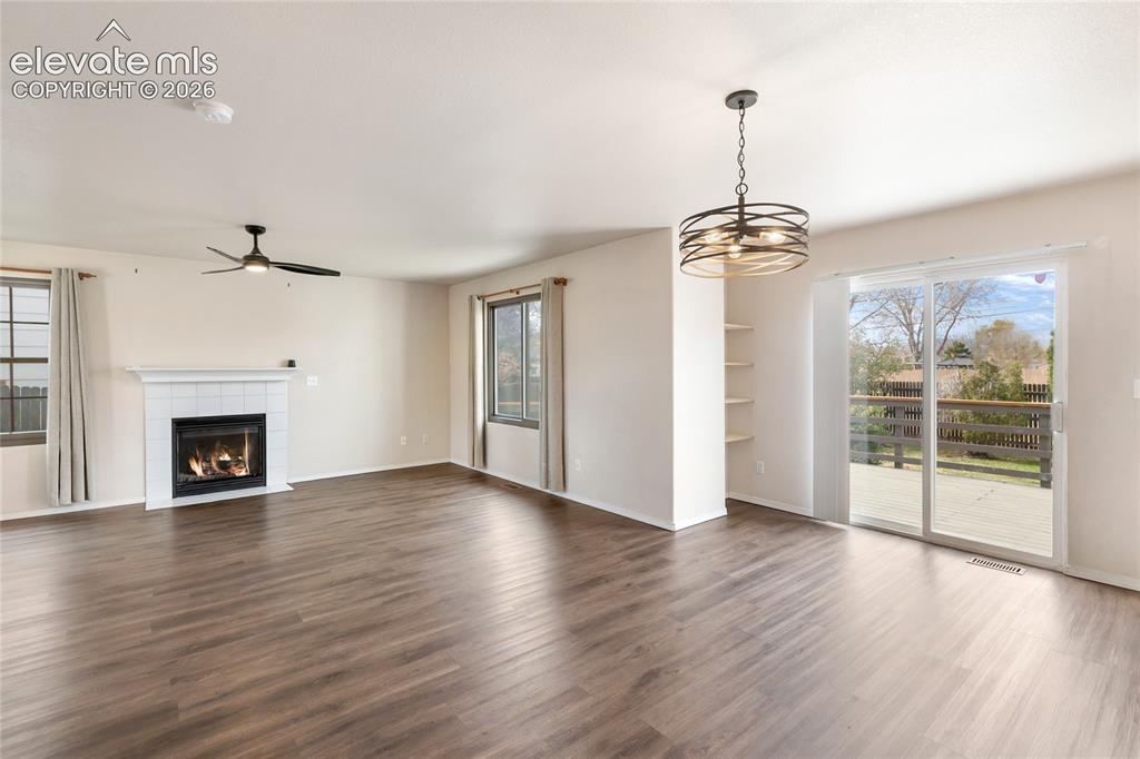 Image 8 of 38: Spacious living area featuring wood-finish flooring, a white-tiled fireplac
