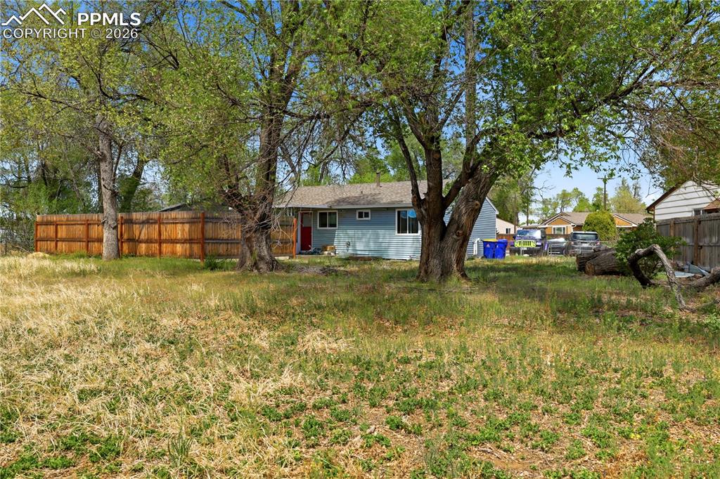 Image 15 of 19: The property features a spacious yard with mature trees and a wooden fence