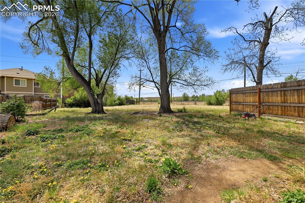 Image 17 of 19: The property features a spacious yard with mature trees and a wooden fence