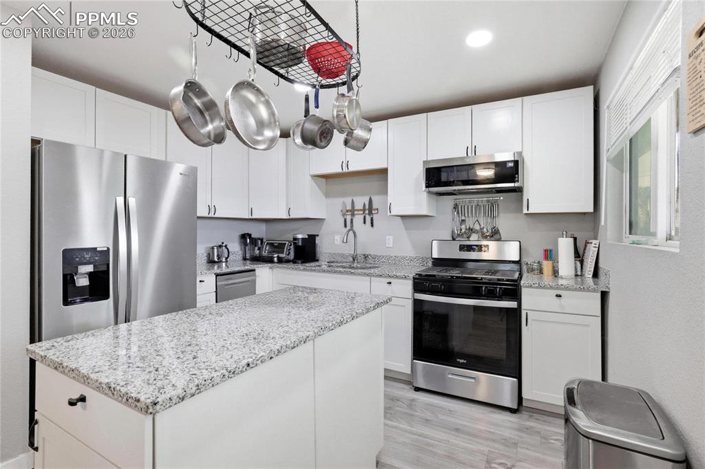 Image 4 of 19: The kitchen features an island with a granite countertop, white cabinetry, 