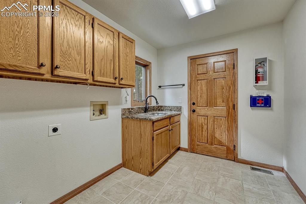 Image 22 of 50: The Laundry Room features upper cabinetry, a sink, window, and access to an