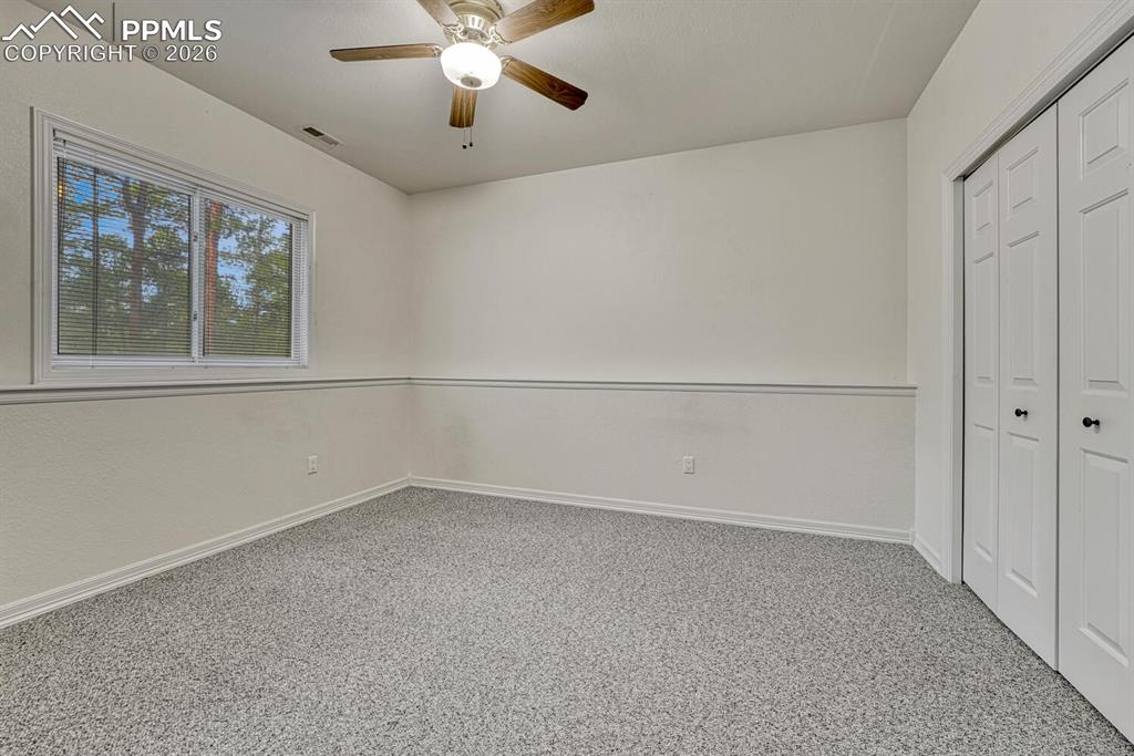 Image 40 of 50: Basement Bedroom #5 has neutral carpet, a lighted ceiling fan, and generous