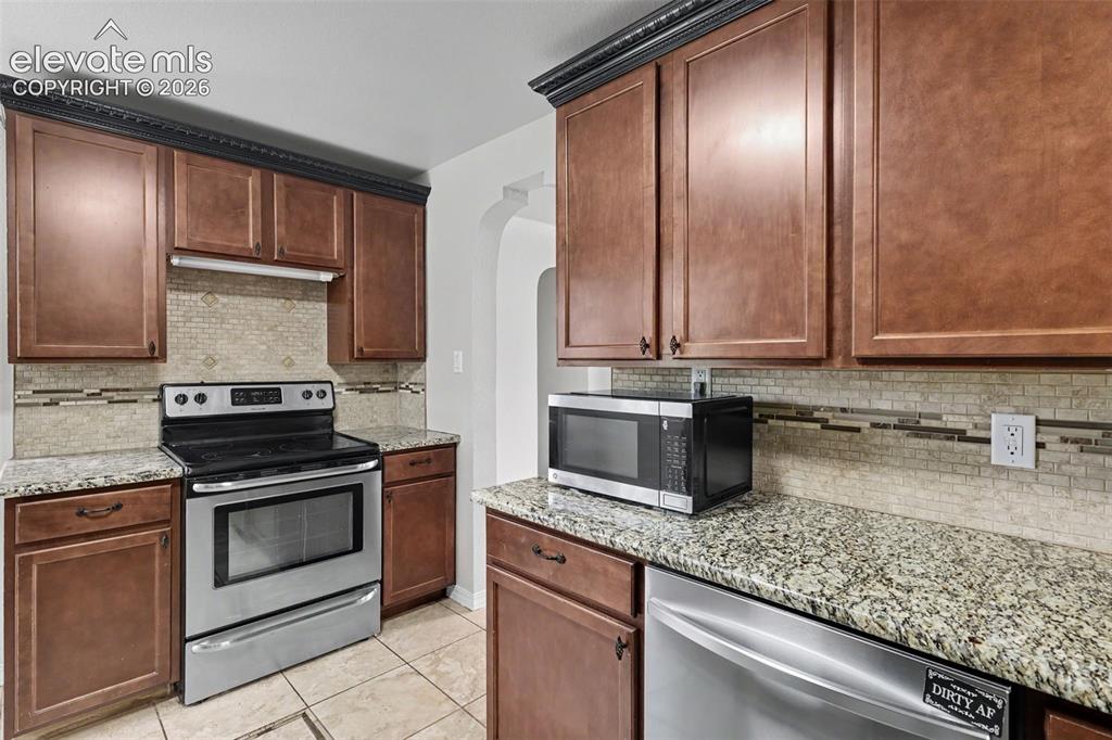 Image 9 of 36: Kitchen featuring wood cabinetry, granite countertops, tile flooring, and a