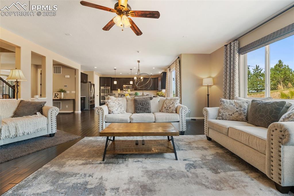 Image 16 of 46: Living room with dark wood-style floors, ceiling fan, a chandelier, and sta