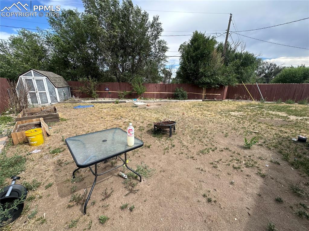 Image 12 of 13: Fenced backyard featuring a shed and an outdoor fire pit