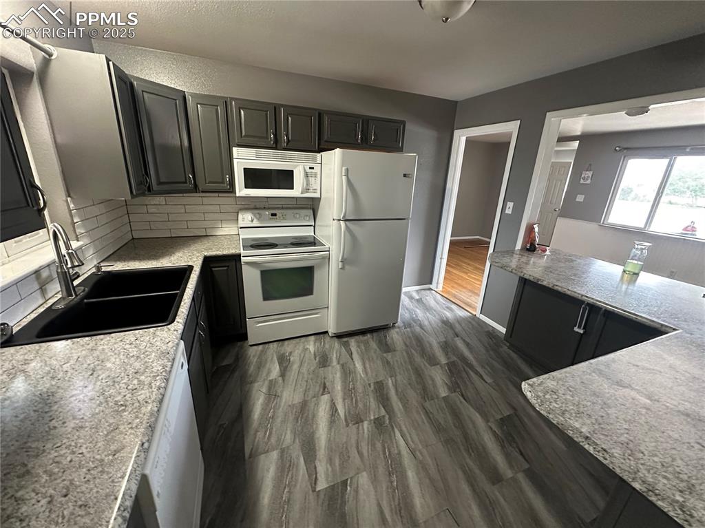 Image 4 of 13: Kitchen featuring white appliances, backsplash, dark wood-style floors, and