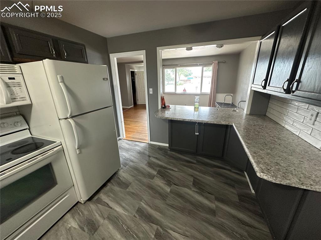 Image 5 of 13: Kitchen featuring white electric stove, dark cabinetry, decorative backspla