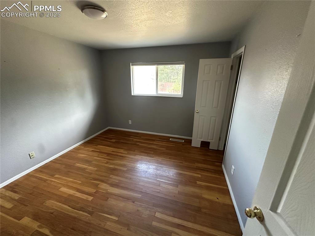 Image 6 of 13: Unfurnished bedroom with a textured wall, a textured ceiling, and wood fini