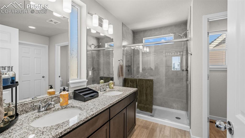 Image 20 of 37: Full bath featuring double vanity, a shower stall, and light wood-style flo