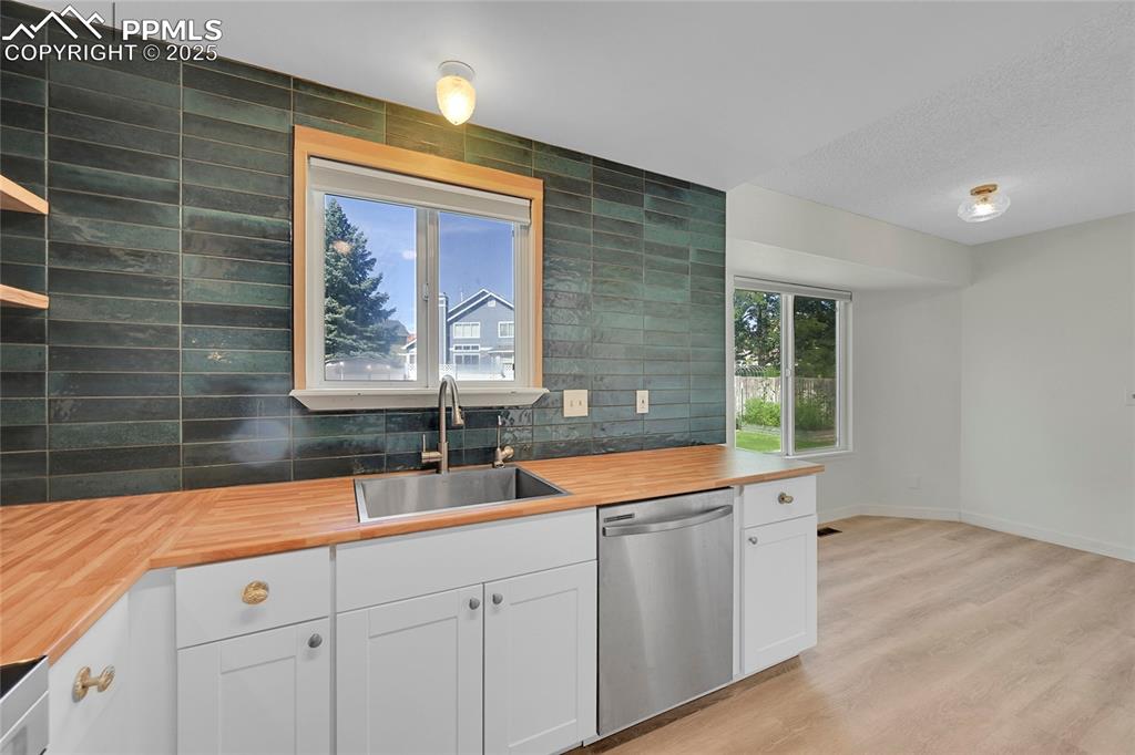 Image 15 of 39: Kitchen with white cabinets, decorative backsplash, stainless steel dishwas