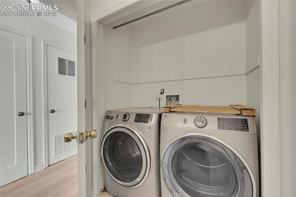 Image 19 of 39: Laundry area with wood finished floors and independent washer and dryer