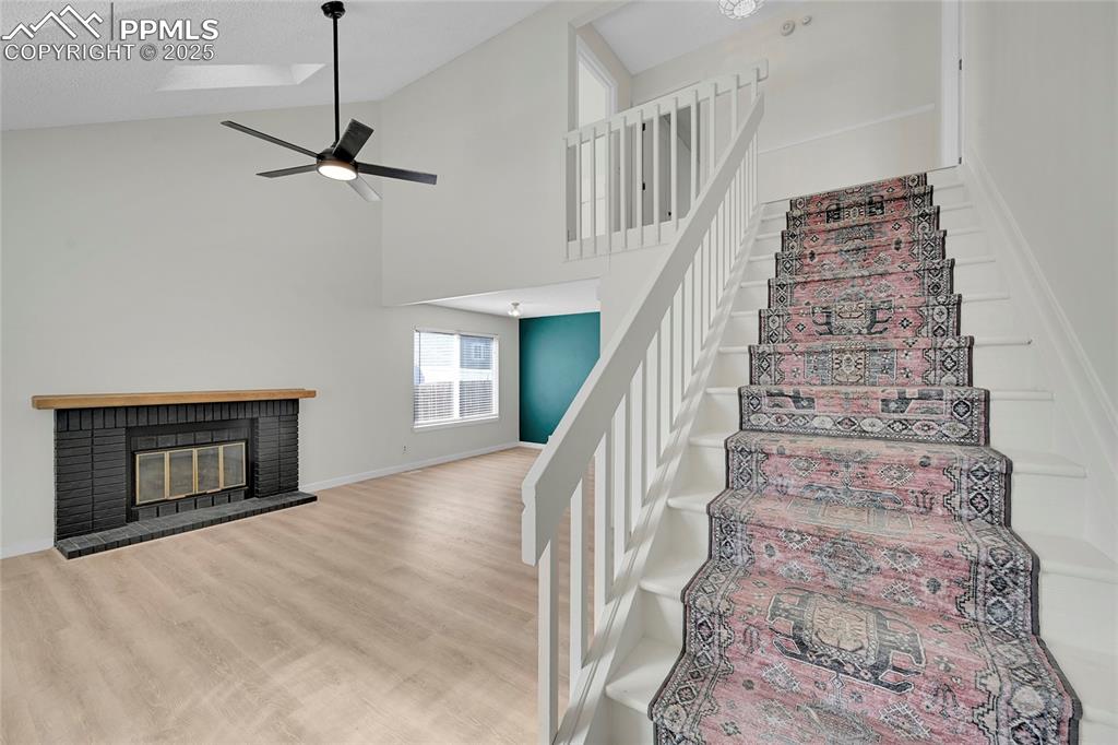 Image 5 of 39: Stairs featuring high vaulted ceiling, wood finished floors, a brick firepl