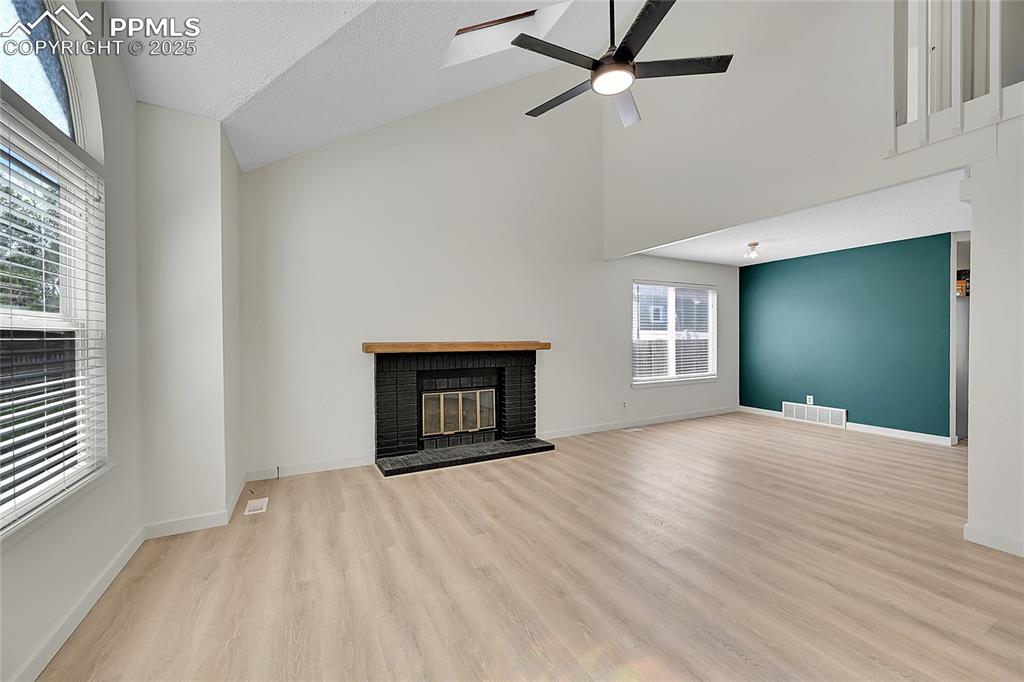 Image 6 of 39: Unfurnished living room with a fireplace, high vaulted ceiling, a ceiling f