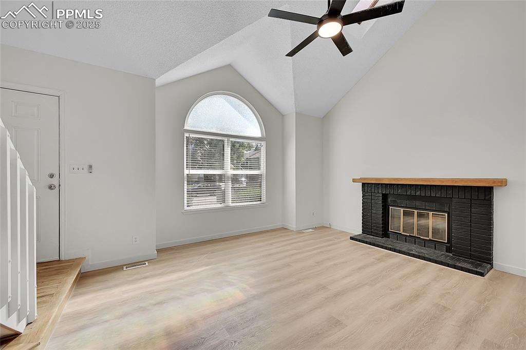 Image 9 of 39: Unfurnished living room featuring lofted ceiling, a fireplace, light wood-s
