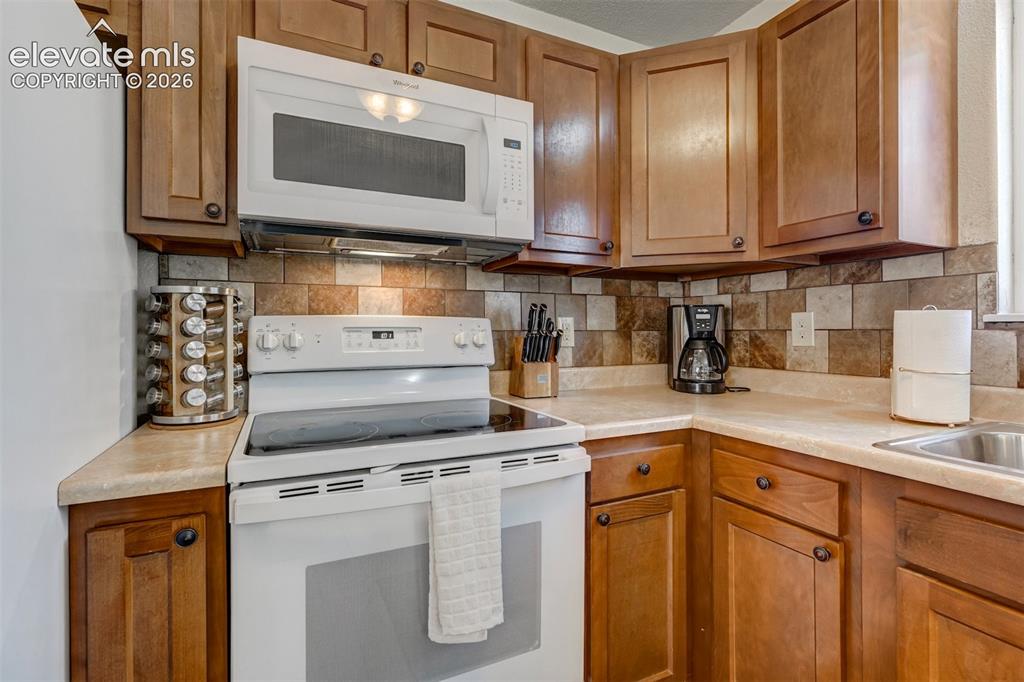 Image 13 of 43: Wood-finish cabinetry, solid surface countertops, tile backsplash, stainles