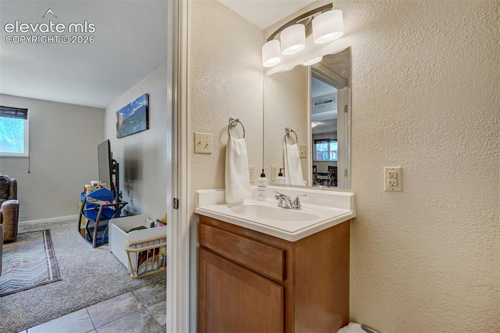 Image 26 of 43: Vanity with wood-finish cabinetry, integrated sink, and wall-mounted light