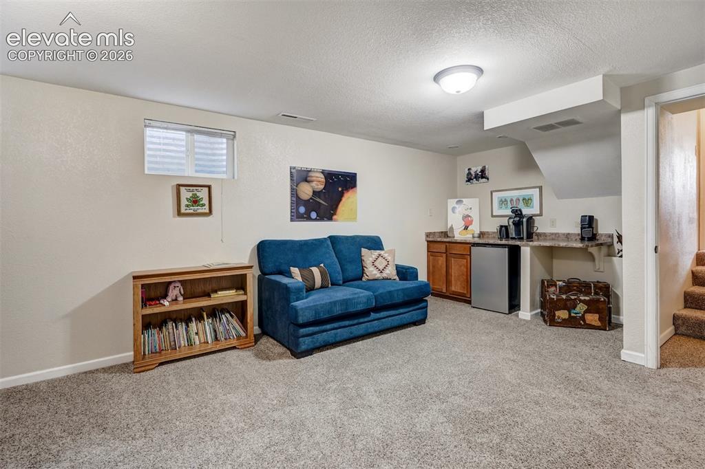 Image 27 of 43: Carpeted room featuring a built-in wet bar with wood-finish cabinetry, a mi