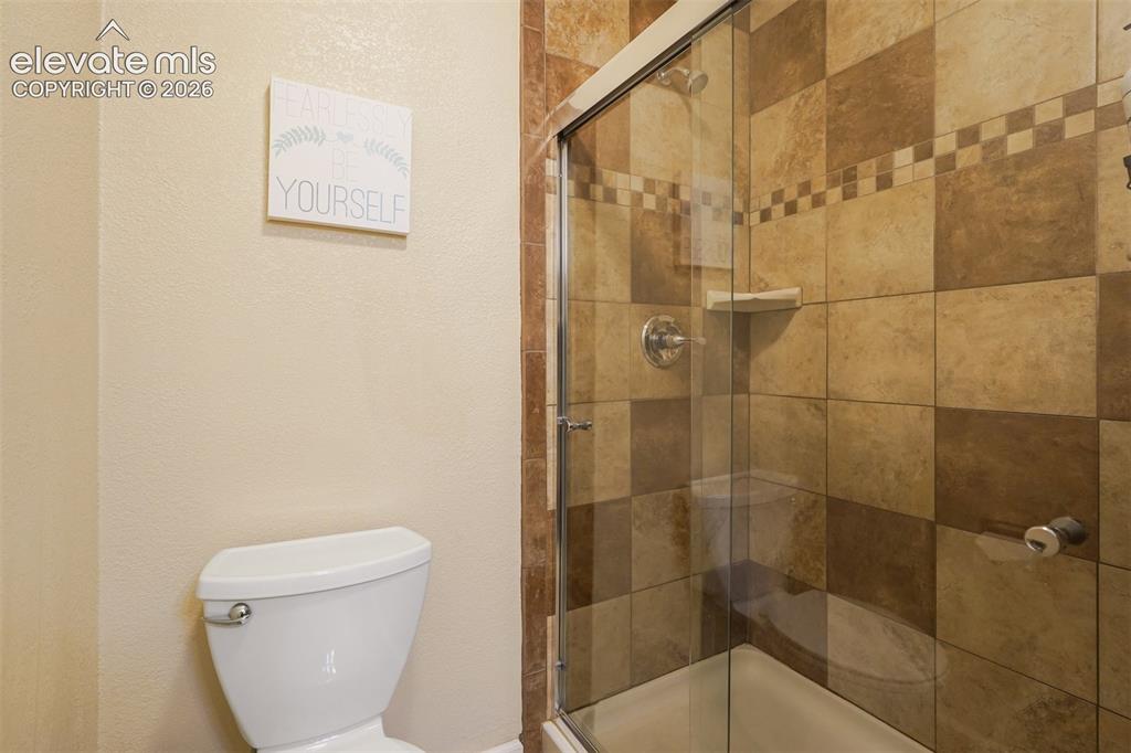 Image 35 of 43: Tiled shower enclosure with a glass door, checkerboard tile pattern, and an