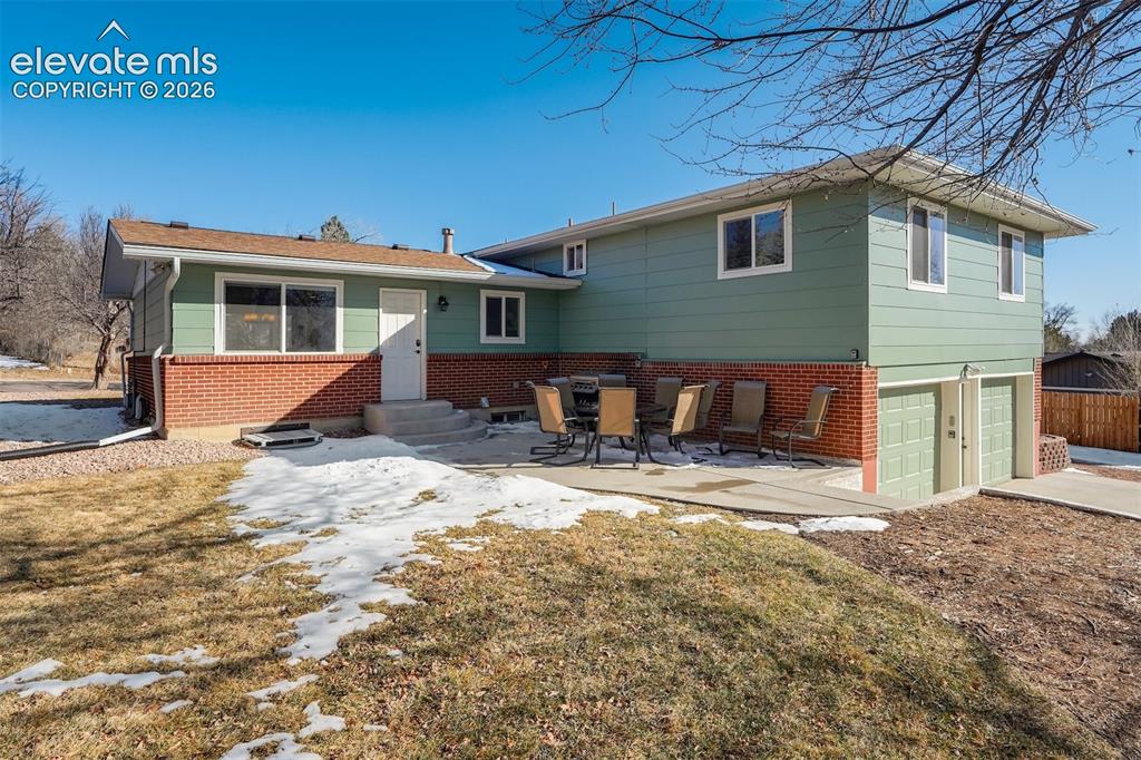 Image 40 of 43: Exterior with green siding, brick accents, concrete patio, and a two-car ga