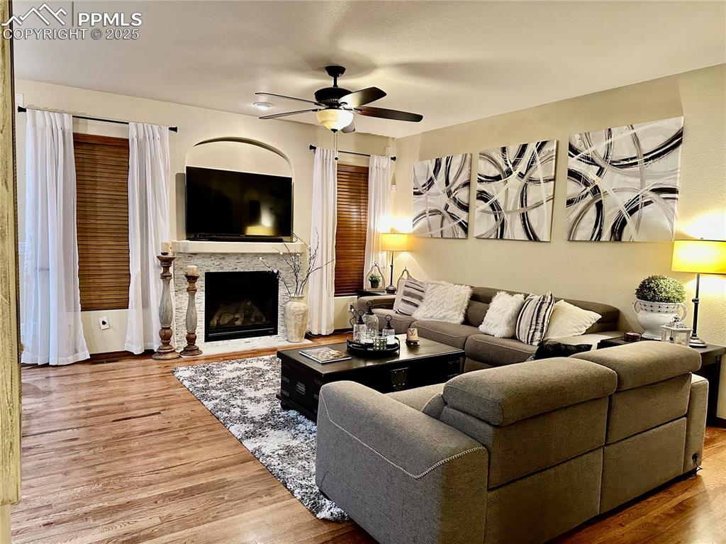 Image 2 of 33: Living area with a fireplace, wood finished floors, and a ceiling fan