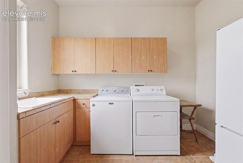 Image 26 of 50: Utility room featuring light wood cabinetry, a built-in sink, and tiled cou