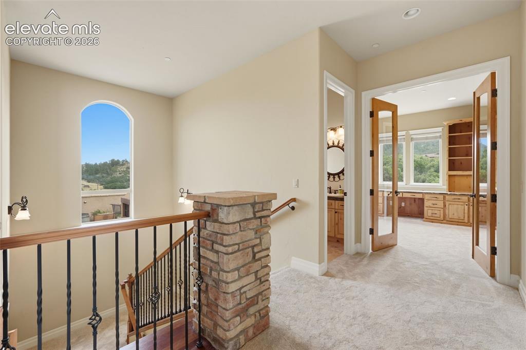 Image 27 of 50: Upper-level landing featuring a stone pillar, wrought iron railing with woo
