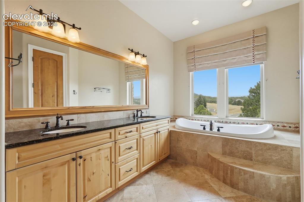 Image 36 of 50: Bathroom featuring a built-in tub with tile surround, dual vanity with dark