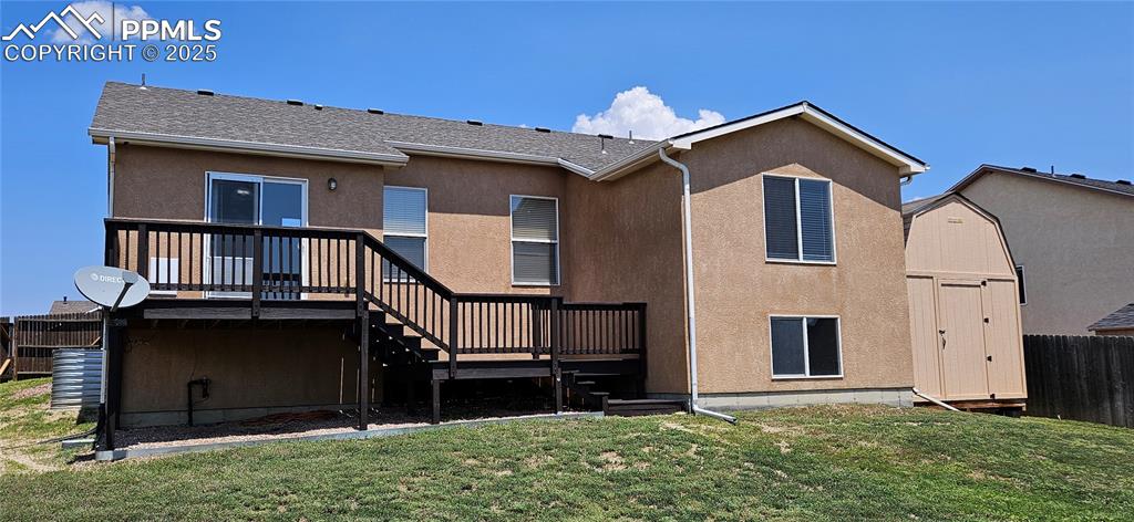 Image 4 of 26: Rear view of house featuring a deck, stairway, a storage unit, and stucco s