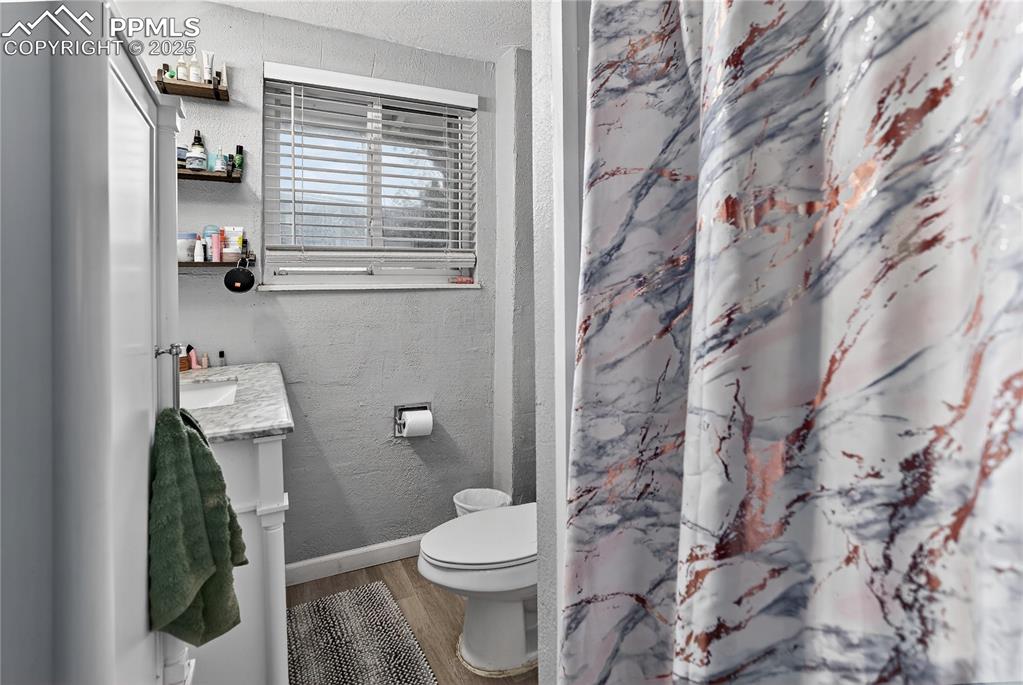 Image 10 of 50: Full main level bath with  textured walls, vanity, light wood-style floorin