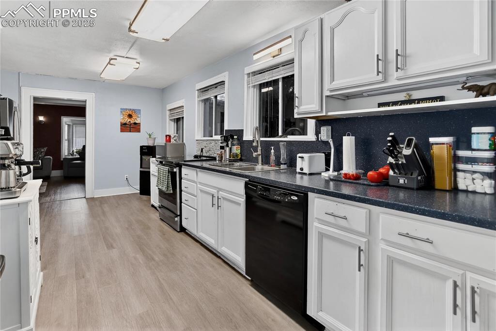 Image 30 of 50: Kitchen featuring dark countertops, electric range, dishwasher, light wood-