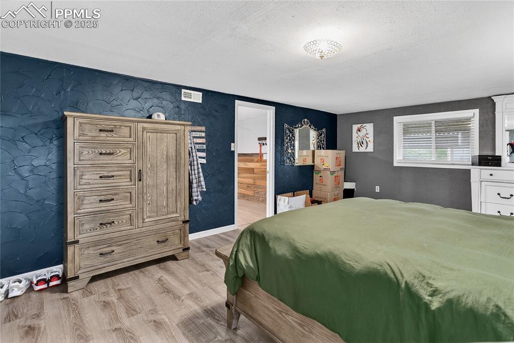 Image 40 of 50: Bedroom with a textured ceiling, light wood-style floors, a textured wall, 