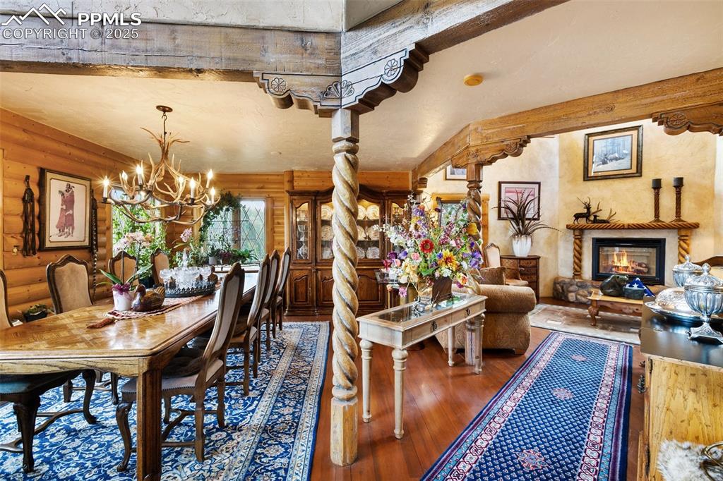 Image 11 of 50: Dining room with log walls, wood-type flooring, a chandelier, and a glass c