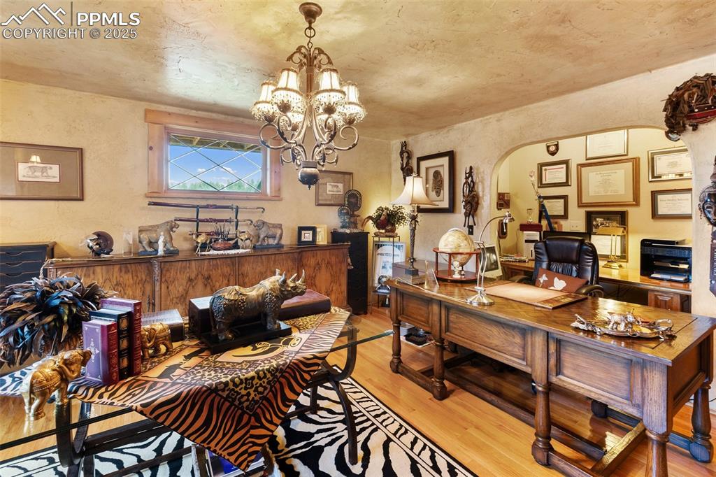 Image 21 of 50: Office space with wood finished floors, arched walkways, a chandelier, and