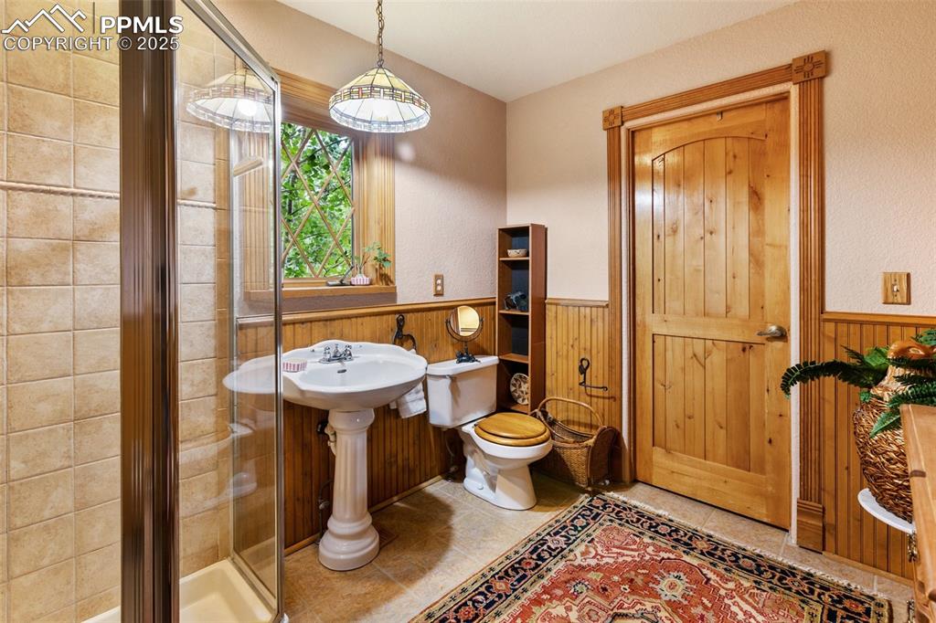 Image 22 of 50: Full bathroom with a wainscoted wall, a stall shower, and wooden walls
