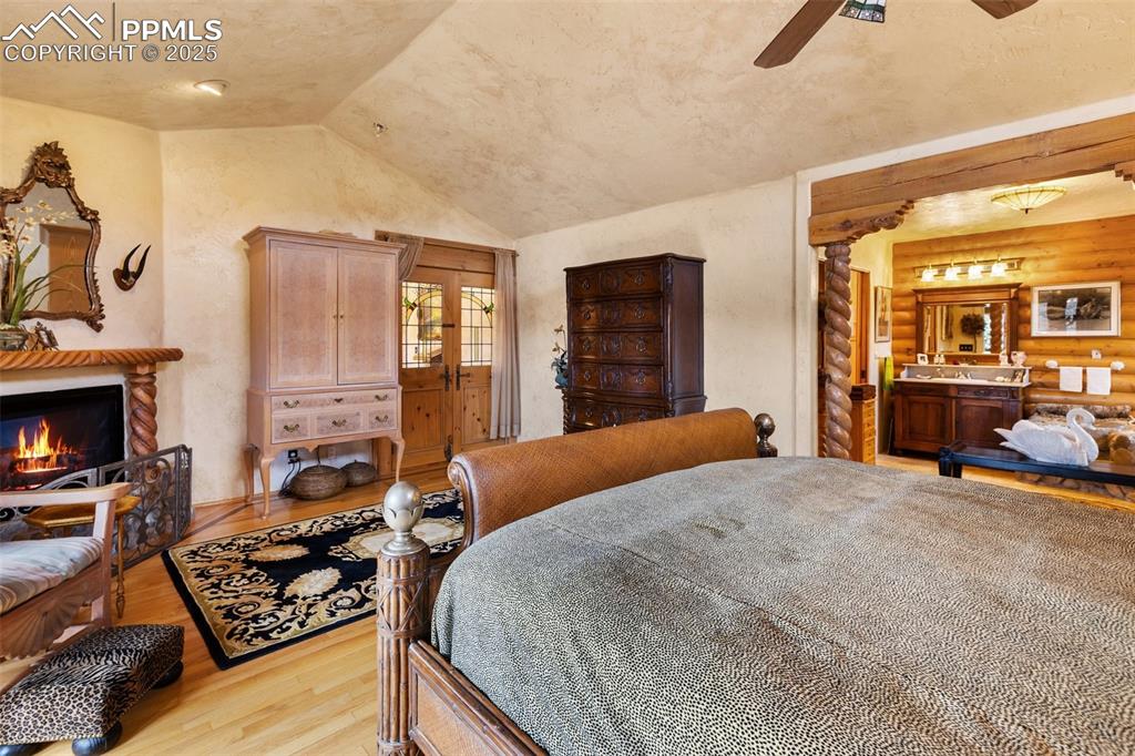 Image 39 of 50: Bedroom featuring wood finished floors, log walls, lofted ceiling, a lit fi