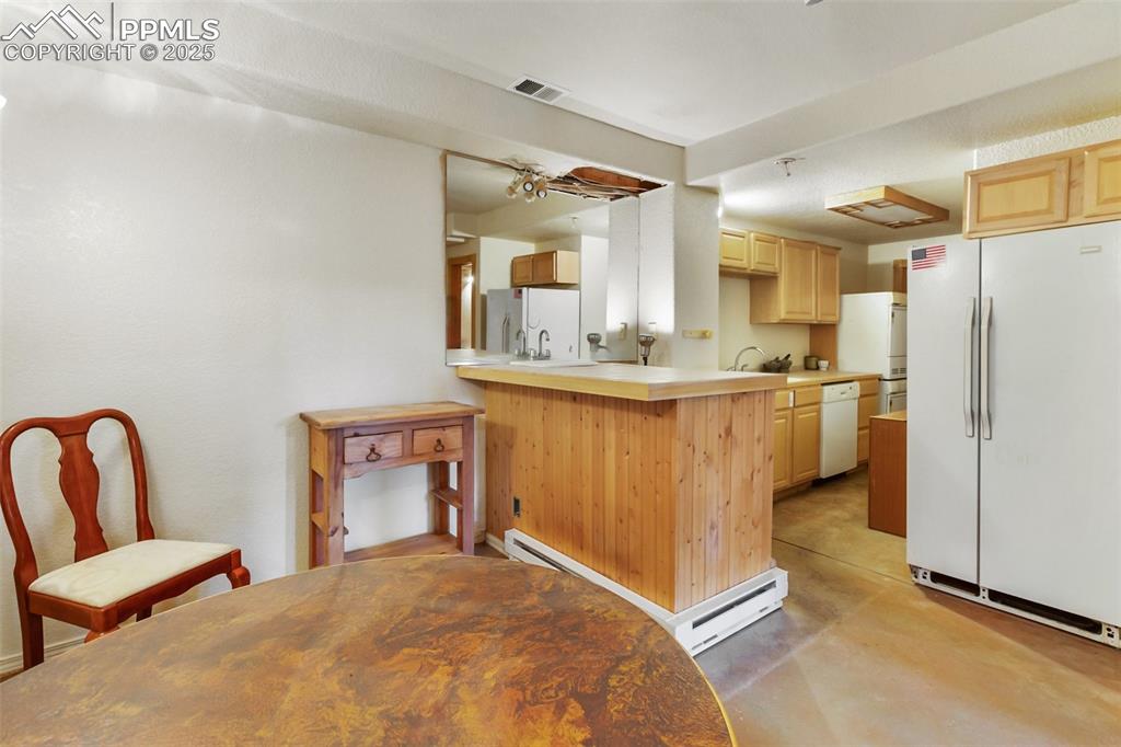 Image 45 of 50: Kitchen with white appliances, light brown cabinets, finished concrete floo