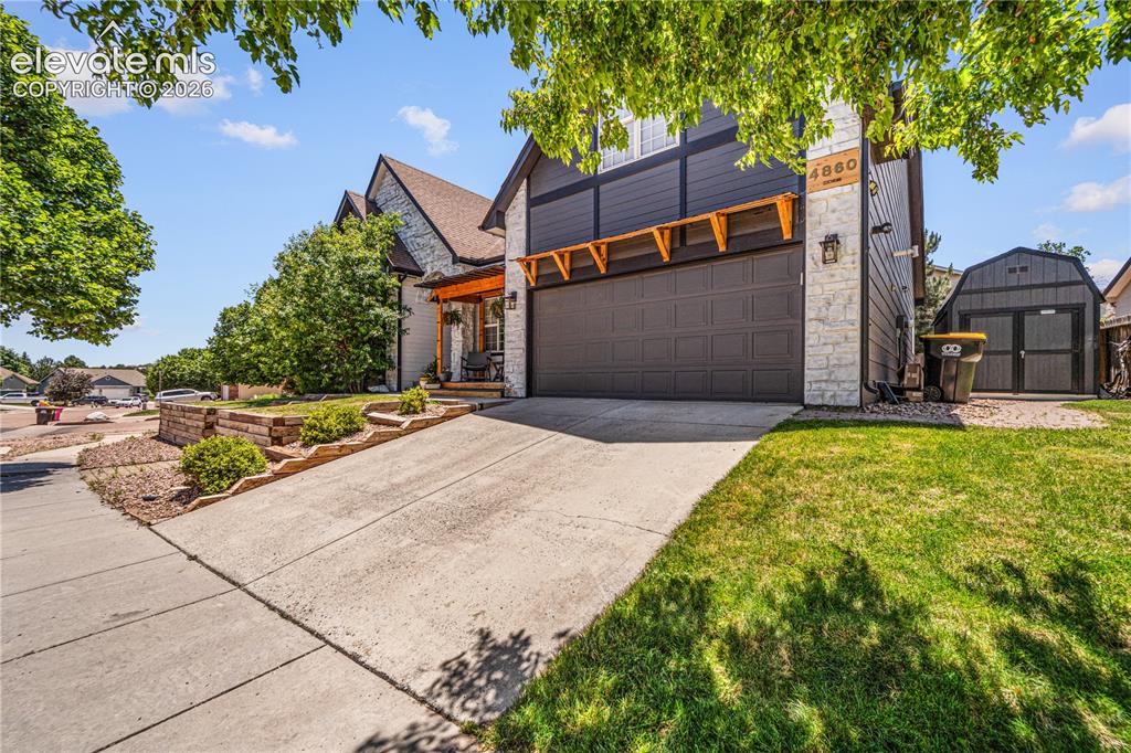 Image 2 of 50: Exterior featuring stone and dark siding, a two-car garage, and a covered f