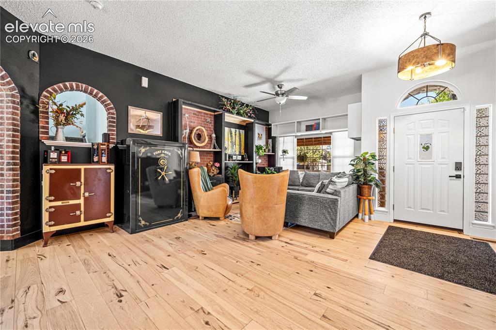 Image 9 of 50: Arched window with blinds and drapes, ceiling fan with light fixture, gray