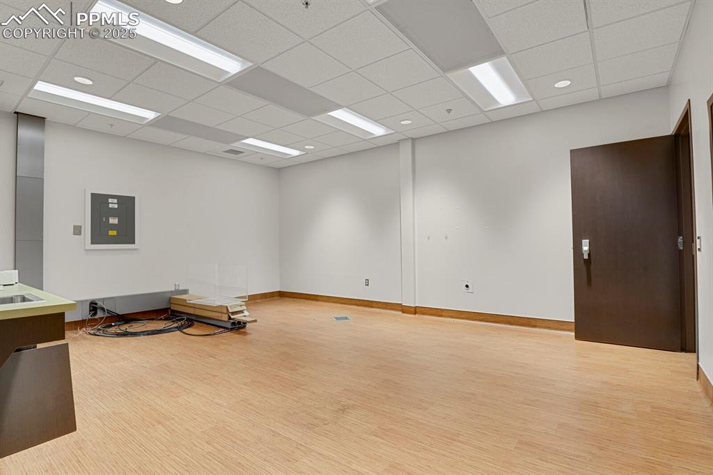 Image 9 of 43: Empty room with light wood-style floors, electric panel, and a drop ceiling