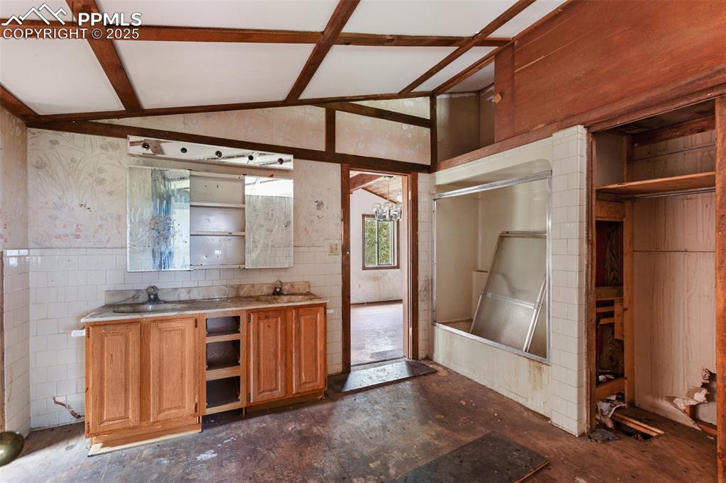 Image 19 of 36: Bar featuring a wainscoted wall, lofted ceiling, and tile walls