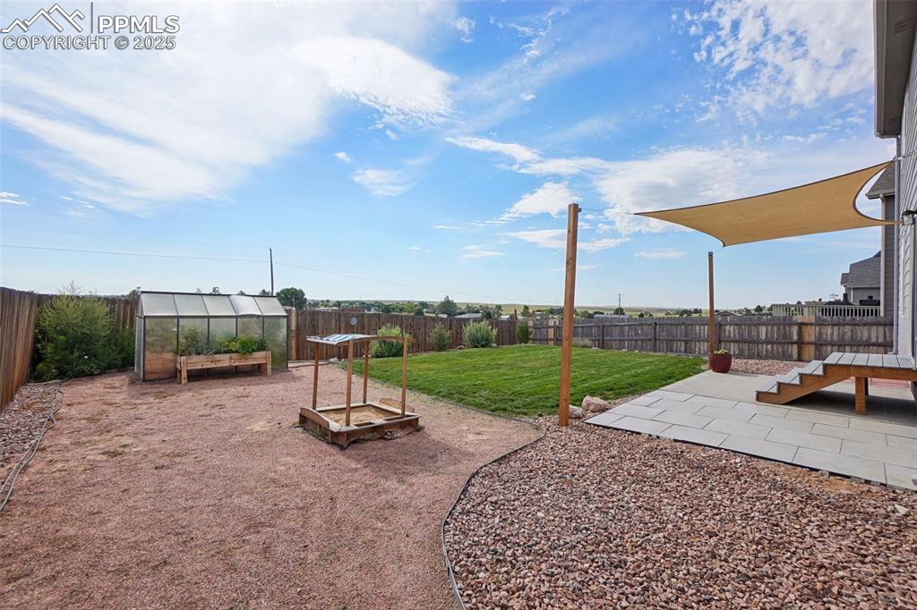 Image 40 of 46: Fenced backyard featuring a garden, a patio, a greenhouse, and an outbuildi