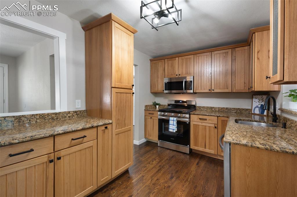 Image 10 of 33: Kitchen with stainless steel appliances, light stone counters, dark wood fi
