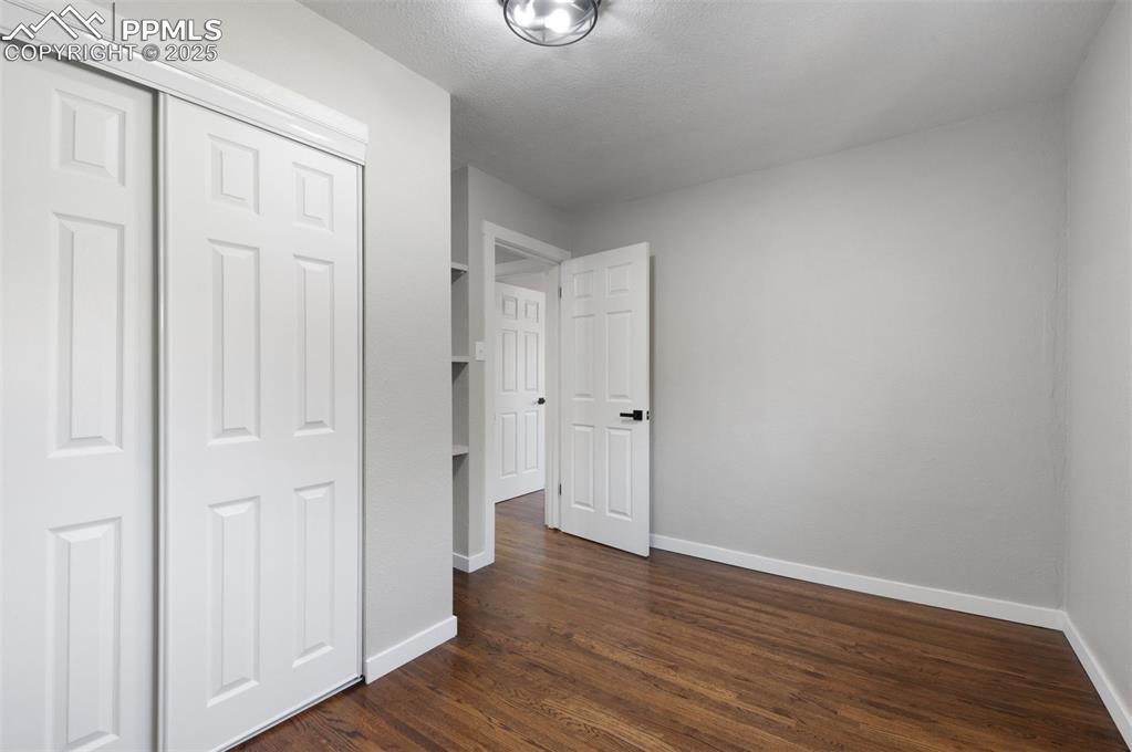 Image 19 of 33: Unfurnished bedroom featuring dark wood-style flooring, a closet, and a tex