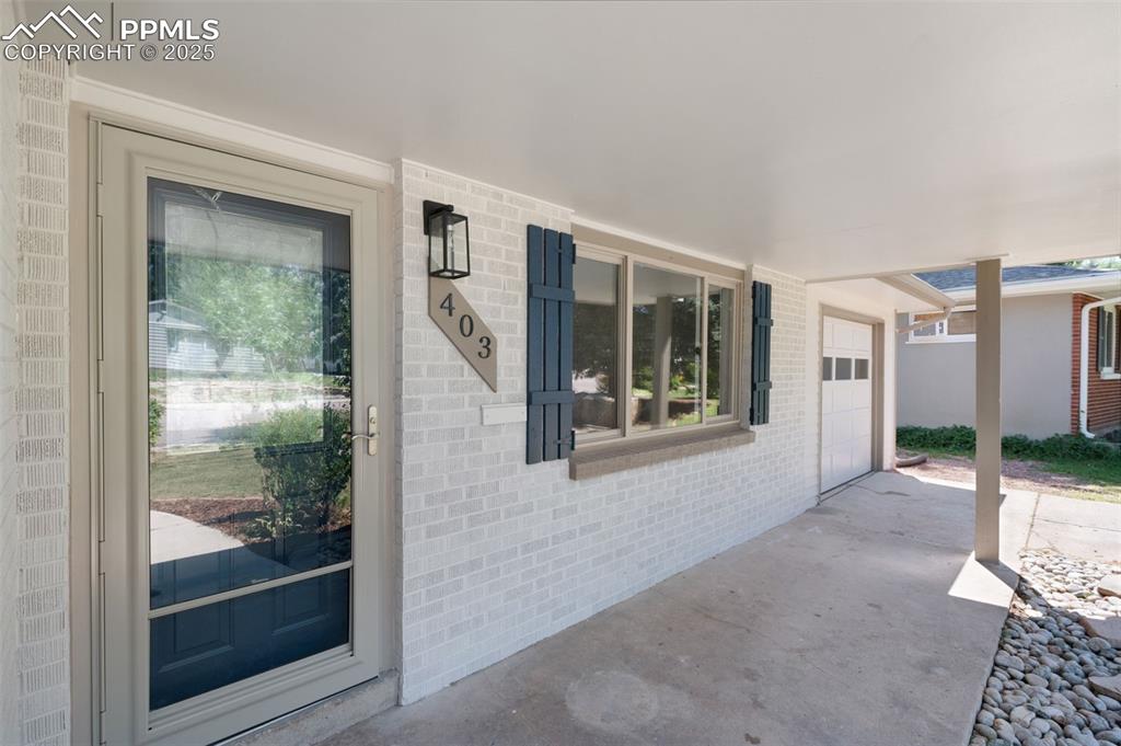 Image 3 of 33: Doorway to property featuring brick siding, a porch, a garage, and driveway