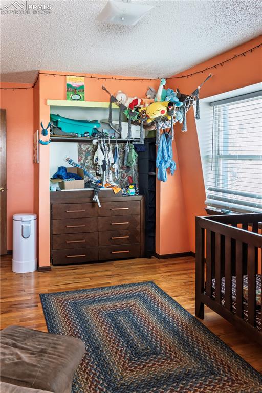 Image 13 of 23: Bedroom with a textured ceiling, light wood-style floors, and a nursery are