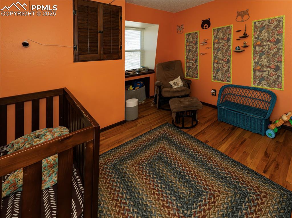 Image 14 of 23: Bedroom with wood finished floors, a textured ceiling, and a nursery area