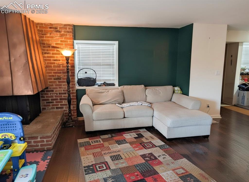Image 4 of 23: Living room featuring dark wood finished floors, brick wall, and plenty of