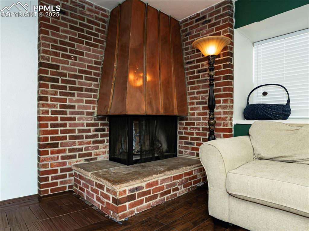 Image 6 of 23: Living room with a fireplace, dark wood-type flooring, and brick wall