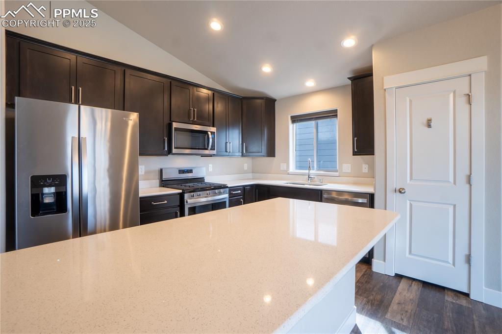 Image 14 of 35: Kitchen featuring stainless steel appliances, dark brown cabinetry, dark wo
