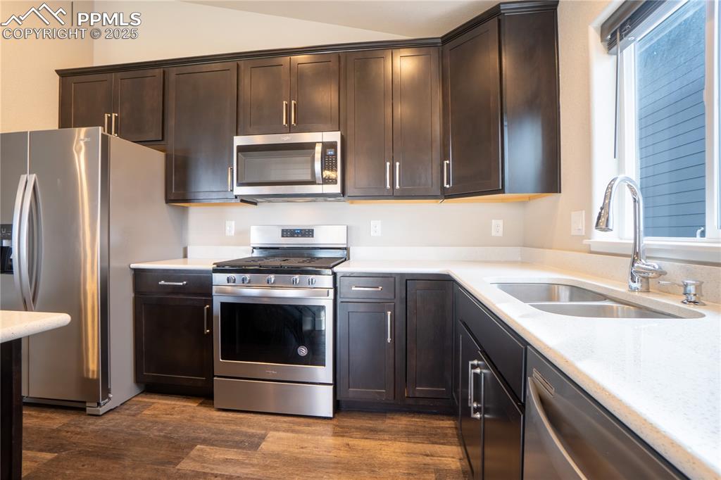 Image 16 of 35: Kitchen featuring stainless steel appliances, dark brown cabinets, dark woo